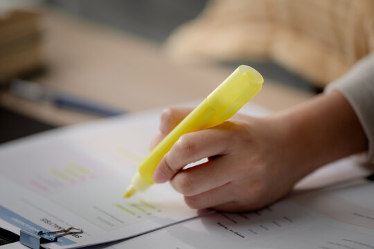 Exam preparation concept. Student highlighting important information while studying with printed documents and a laptop at home for online learning and test revision. Study, exam, highlight, learning,