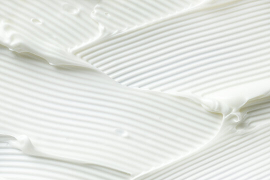White cosmetic cream texture background. Macro full frame of skincare lotion smear with ribbed pattern. Creamy moisturizing lotion smear background for skincare design.