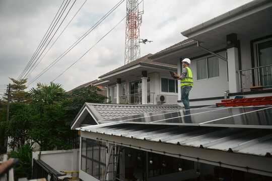 Engineer Inspecting Rooftop Solar Panels Using Drone and Laptop on Residential House