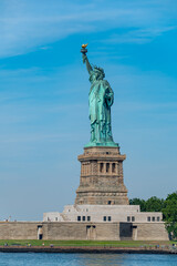 Front view of the Statue of Liberty in New York. Green copper sculpture standing on a stone pedestal against a vibrant sky with wispy clouds. © Vadim