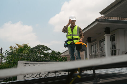 Solar Panel Technician Standing on Residential Rooftop During Installation with Tool Box and Safety Gear