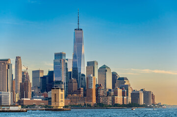 Fototapeta premium Lower Manhattan skyline and One World Trade Center from the river. Skyscrapers of downtown district and small ferry on water during late afternoon.