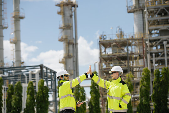 Engineers celebrating achievement with high five at construction site of industrial plant showcasing teamwork and safety measures