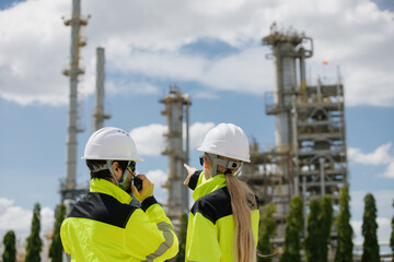 Fototapeta premium Engineers collaborating on project blueprints at a construction site surrounded by heavy machinery and industrial structures