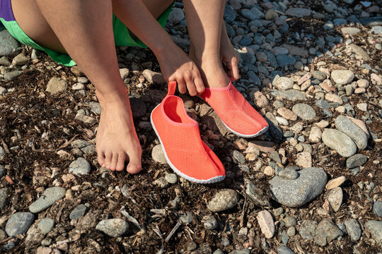 Person putting on coral water shoes on a rocky beach