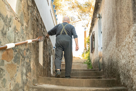 Elderly man climbing stone steps in Palamos alleyway