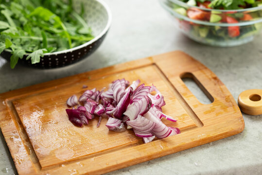 Chopped red onion on wooden board with salad bowls