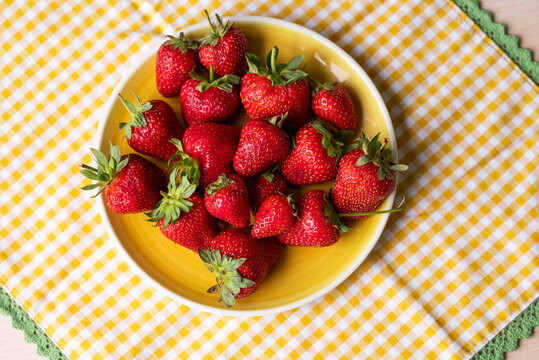 Fresh strawberry on yellow plate on checkered cloth