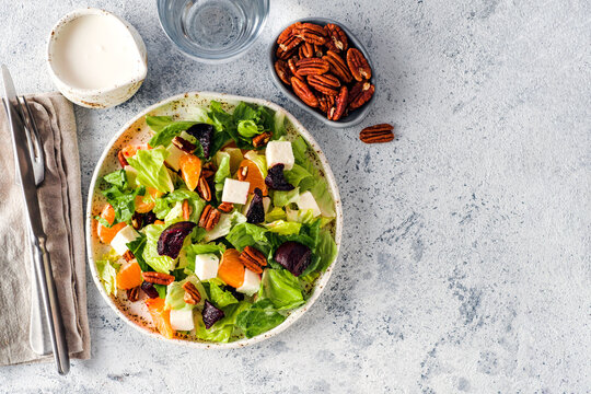 Healthy fresh salad with beet, feta cheese, oranges and pecans. Flat lay composition with cutlery and dressing on bright textured gray concrete background with copy space. Ideal for wellness blog