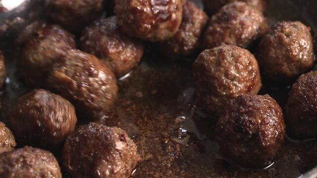 Close-up horizontal video of homemade Italian meatballs gently tossed. Traditional comfort food prepared in a pan.