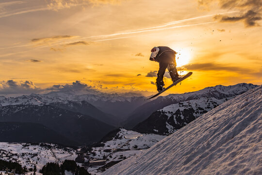 Snowboarder catching air at sunset in snowy mountains