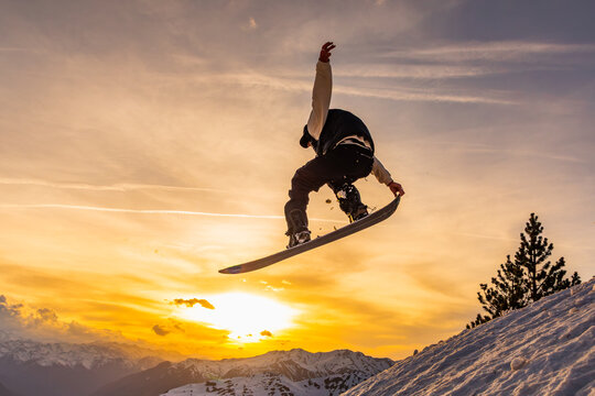 Snowboarder jumping against a sunset mountain backdrop