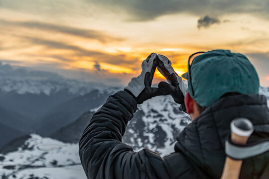 Snowboarder capturing mountain sunset with hand frame