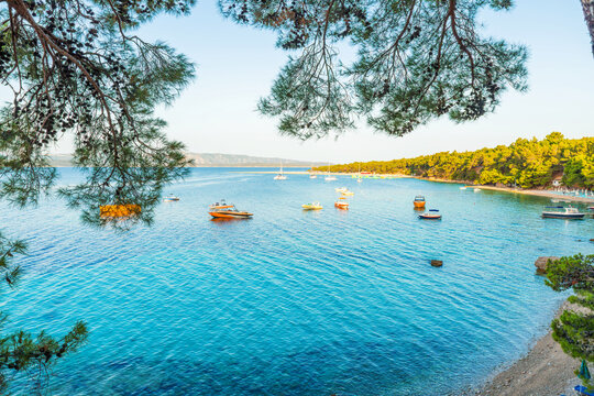 Peaceful bay on Brac island with crystal clear Adriatic sea, Zlatni Rat beach, anchored boats and Mediterranean pine forest coastline, Dalmatia, Croatia. European travel destination, island tourism