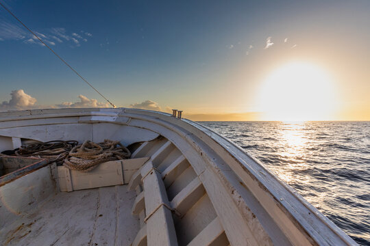 Wooden boat bow at sea during golden sunset horizon