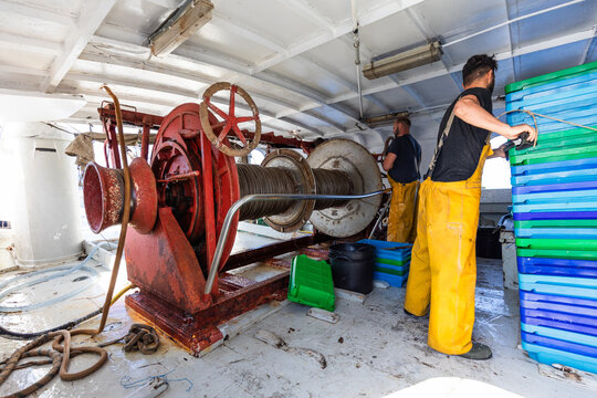 Fishermen working on trawler deck with winch and crates