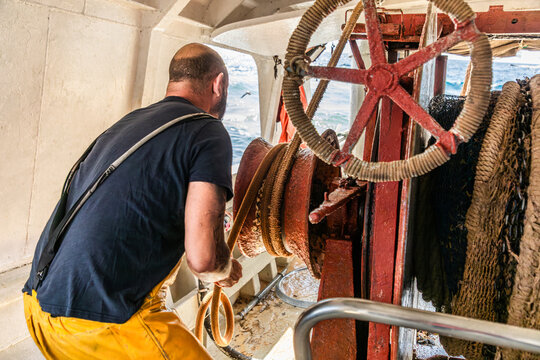 Fisherman operating winch and rope on working fishing boat
