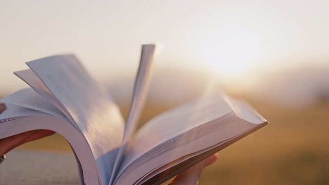 Hand flipping through pages of old open book in warm golden sunset light. Close-up of paper moving, peaceful reading atmosphere with cinematic look.
