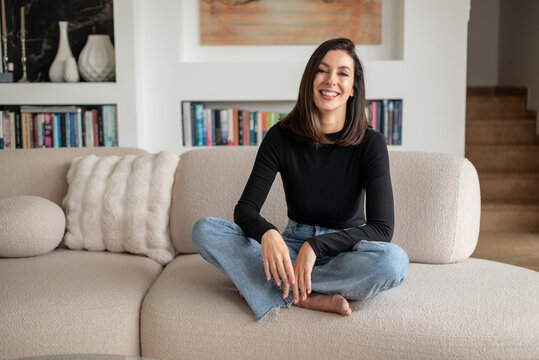 Smiling brunette haired woman relaxing on a sofa in her modern home interior