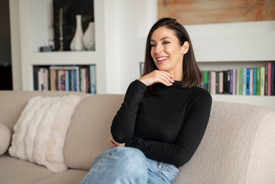 Smiling brunette haired woman relaxing on a sofa in her modern home interior