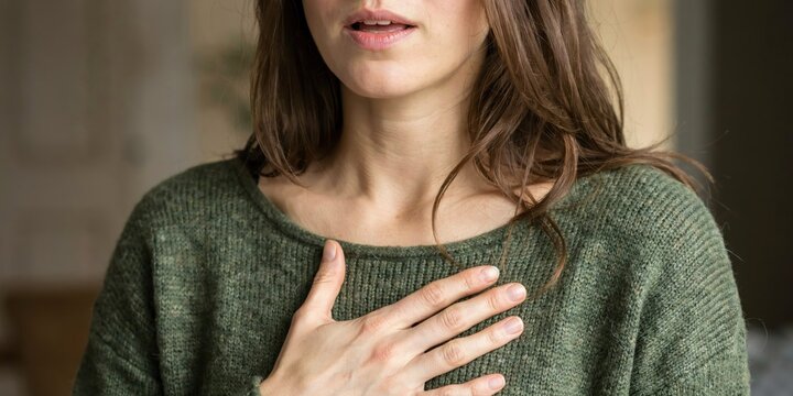 Woman suffering from shortness of breath or chest pain, hand on chest with concerned expression.