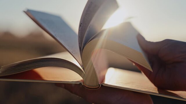 Close-up of an open book. Pages turn in evening sunlight. Paper texture, reading, education, imagination lifelong learning concept