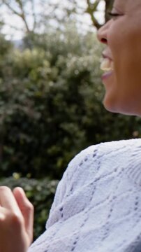 Vertical video: Talking mid-adult woman in sweater laughing at Santa pompom in garden, copy space