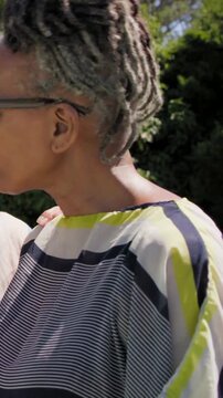 Vertical video: Turning woman locs as friend touching her at park, in top and shades, sipping cup
