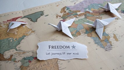 Fototapeta premium Paper cranes on a vintage world map with the word freedom and a message about exploration and the essence of journeying
