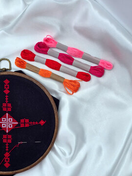 Embroidery process with colorful floss skeins and red cross stitch pattern