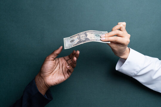 Hand giving dollar bill to another hand on dark background