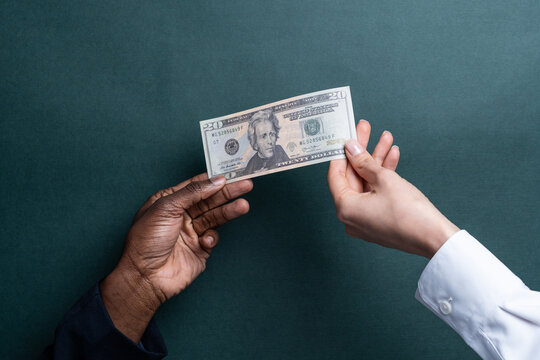 Multiethnic hands exchanging a US twenty-dollar bill