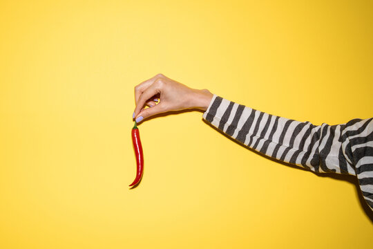 Hand holding red chili pepper on bright yellow background