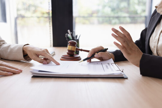 A professional lawyer or legal advisor consulting with a client in a modern office, explaining legal contract terms with a wooden gavel on the table.