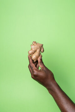 African man hand holding ginger root on green background
