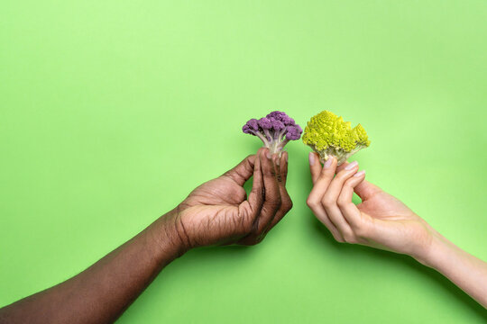 Multiethnic hands holding colorful cauliflower on green