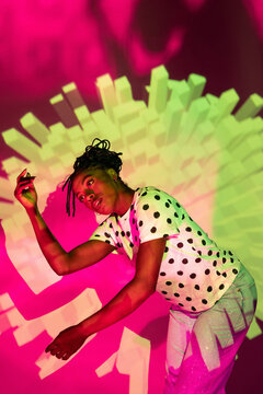 Afro woman dancer in polka dot shirt under neon light