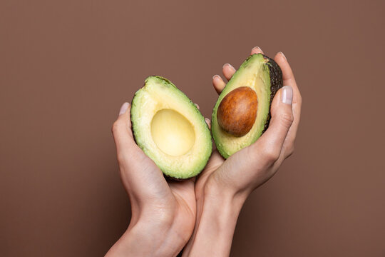 Hands holding halved avocado on brown background