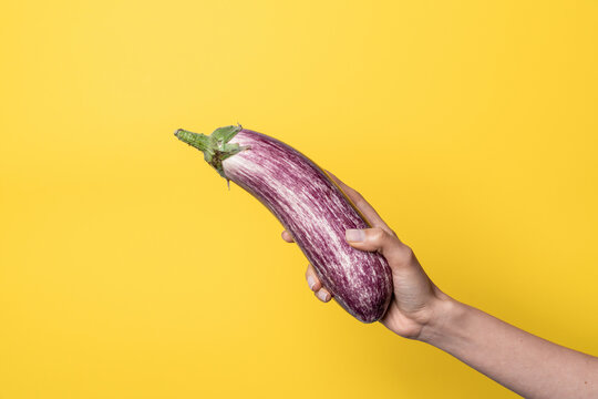 Hand holding eggplant on yellow background sex concept