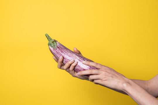 Hands holding eggplant on yellow background, sex concept