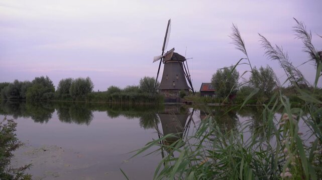 Iconic Windmill at Kinderdijk UNESCO World Heritage Site in the Netherlands, Reflecting in Calm Water on a Cloudy Summer Day.