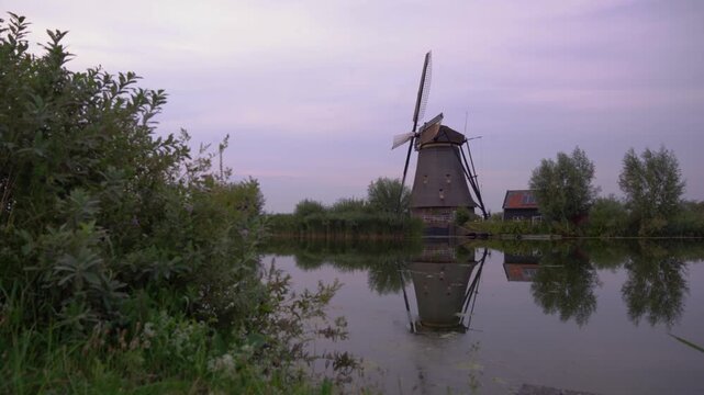 Iconic Windmill at Kinderdijk UNESCO World Heritage Site in the Netherlands, Reflecting in Calm Water on a Cloudy Summer Day.