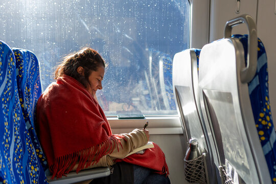 Woman journaling by train window on sunny winter trip