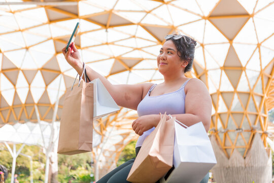 Woman taking selfie with shopping bags under canopy