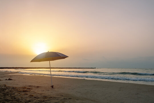 Straw beach umbrella at sunrise on empty sandy beach