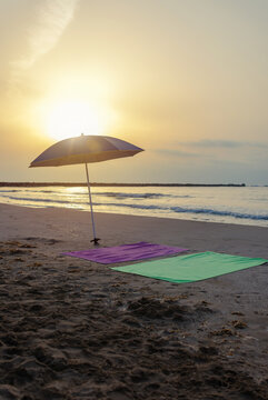 Vertical beach towels beneath straw umbrella at sunrise