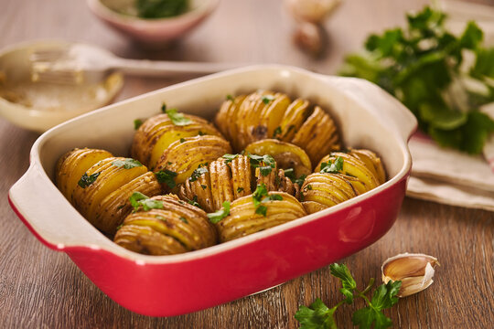 Hasselback roasted potato in baking dish with herbs