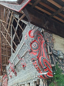 Close up details of traditional red, black, and white Gorga wood carvings and Singa-singa ornament on the exterior wall of a traditional Batak Toba house (Rumah Bolon) in Samosir Island, North Sumatra