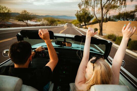 Young couple driving in convertible with hands in the air