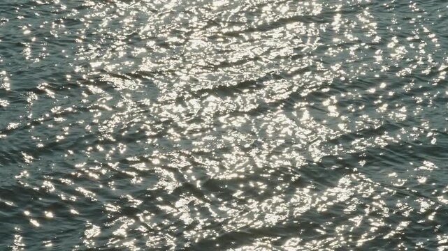  Bright sunbeams create thousands of brilliant sparkles on dark rippling water.